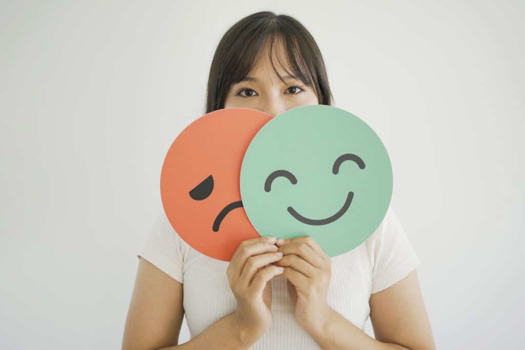 Une femme masquant son visage avec deux smiley, l'un joyeux, l'autre triste
